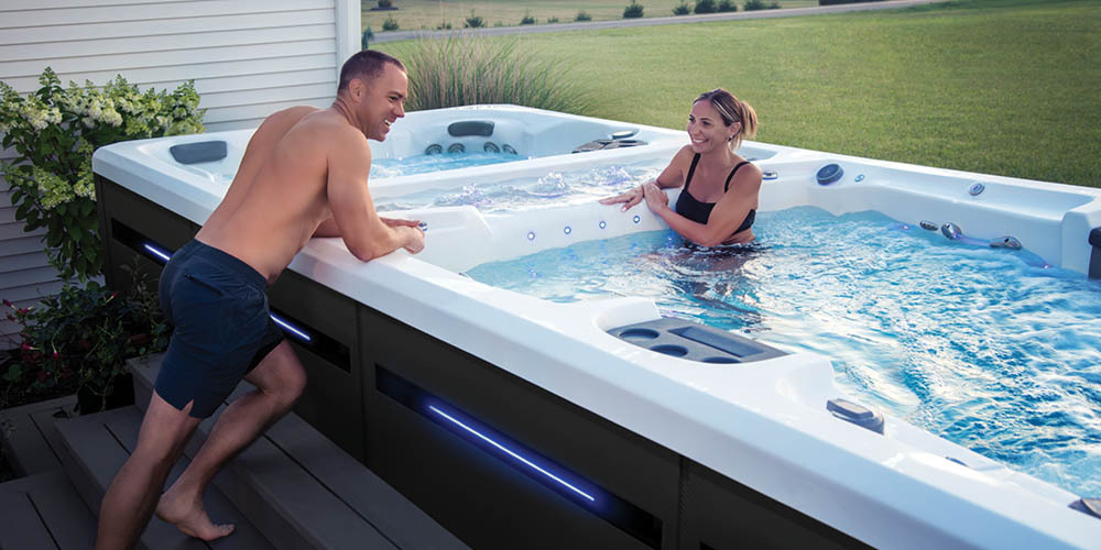 A man leaning over the edge of an H2X swim spa to speak with a woman enjoying the water.